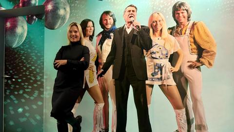 Britta Wiegand lehnt an einer Wand mit einer Fototapete von ABBA und Udo Jürgens