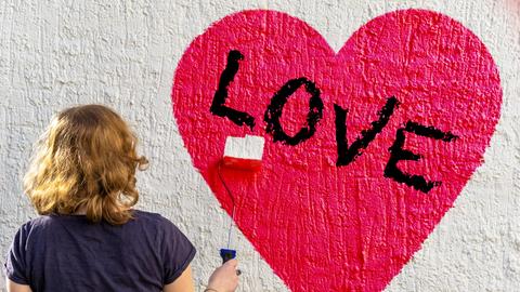 Eine Frau malt ein Herz an eine Wand
