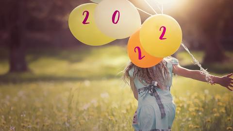 Mädchen  mit Luftballons läuft über eine Wiese. Auf den Ballons stehen die Zahlen 2, 0, 2 und 2.