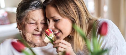 Eine ältere und eine jüngere Frau riechen an einer Tulpenblüte