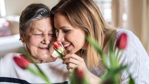 Eine ältere und eine jüngere Frau riechen an einer Tulpenblüte